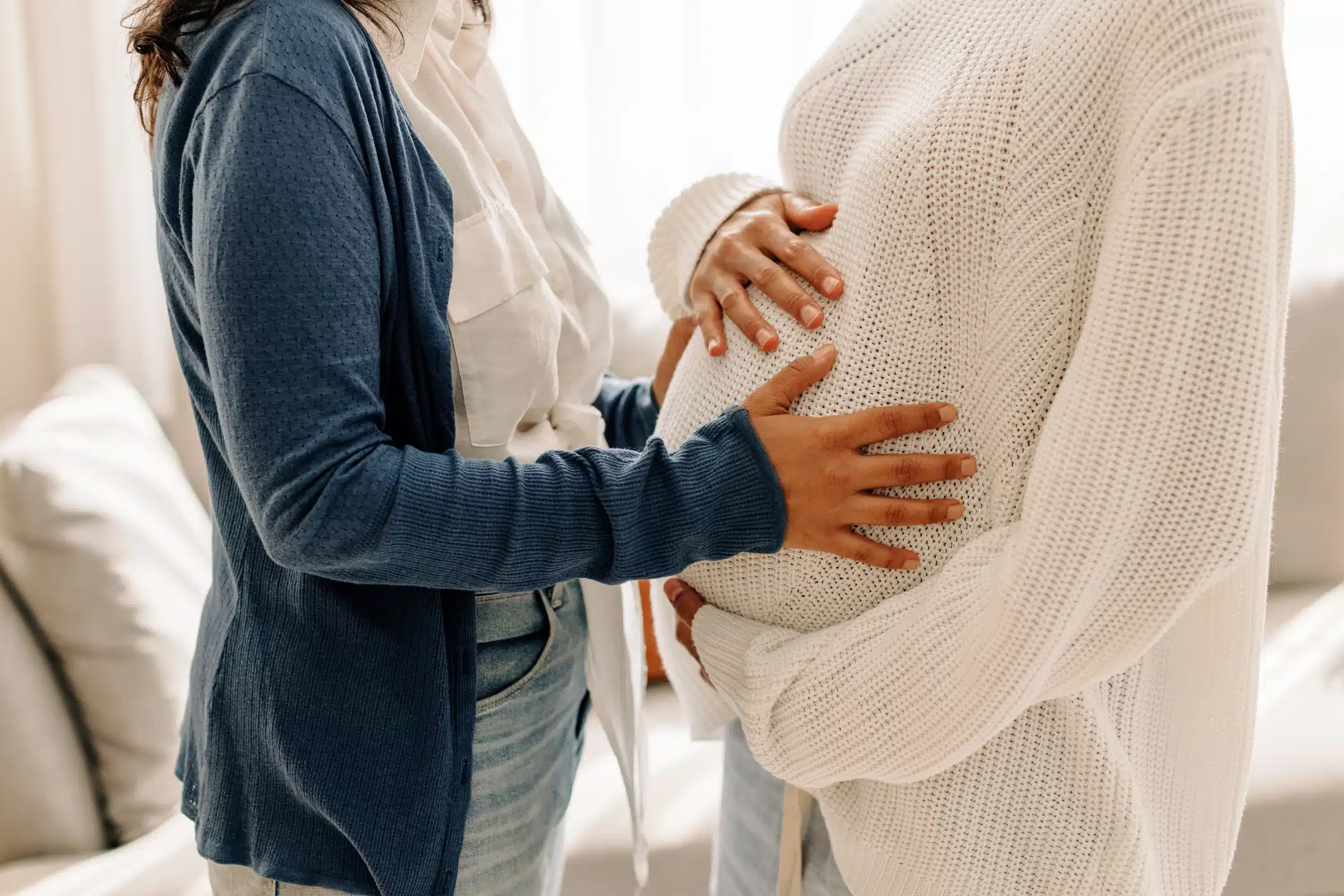 Two women bonding during a pregnancy, touching a baby bump.